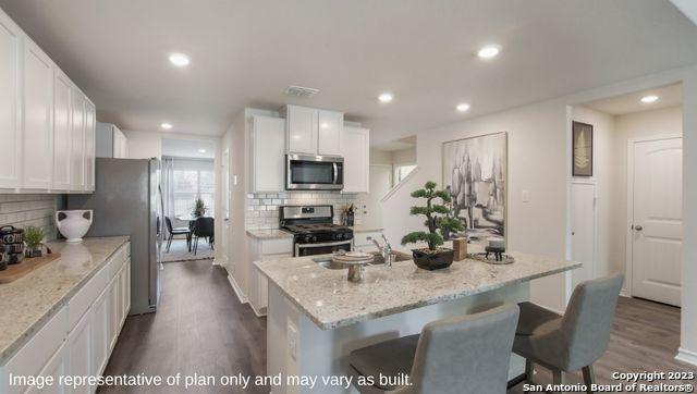 kitchen featuring light stone countertops, appliances with stainless steel finishes, decorative backsplash, a center island with sink, and white cabinetry