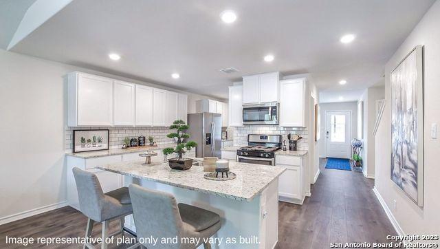 kitchen with white cabinetry, light stone countertops, a breakfast bar area, a kitchen island, and appliances with stainless steel finishes