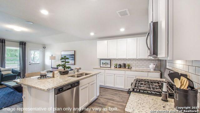 kitchen featuring dishwasher, a center island with sink, sink, light stone countertops, and white cabinetry