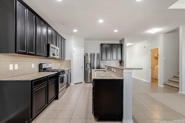 kitchen with light stone countertops, light tile patterned floors, stainless steel appliances, and an island with sink