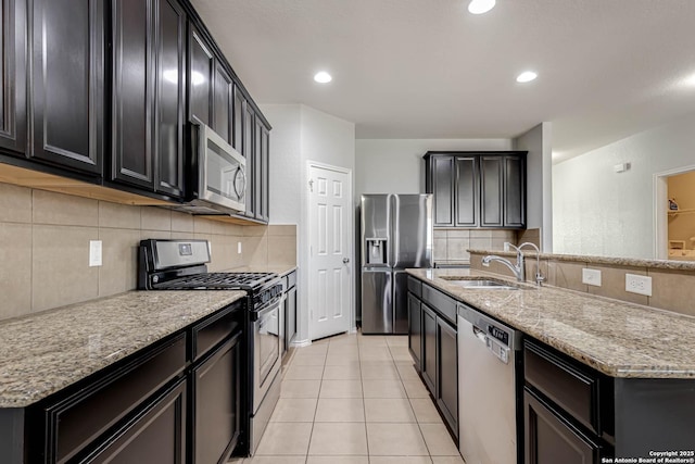 kitchen featuring sink, stainless steel appliances, light stone counters, an island with sink, and light tile patterned flooring