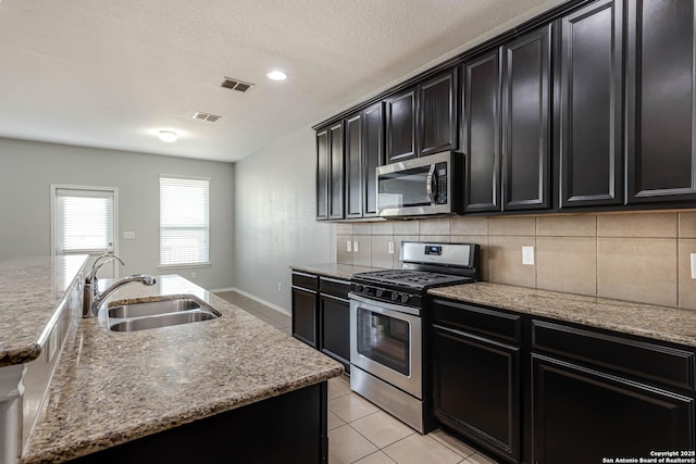 kitchen featuring light stone countertops, sink, backsplash, a kitchen island with sink, and appliances with stainless steel finishes