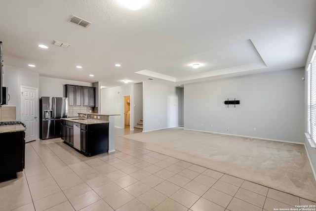 kitchen featuring light colored carpet, sink, a tray ceiling, light stone counters, and stainless steel appliances