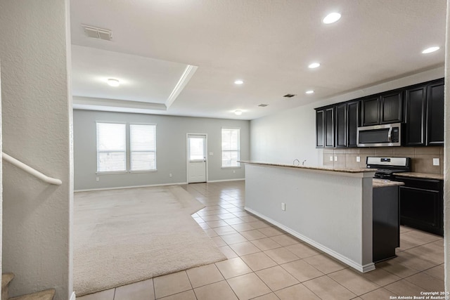 kitchen with gas stove, a raised ceiling, an island with sink, decorative backsplash, and light tile patterned floors