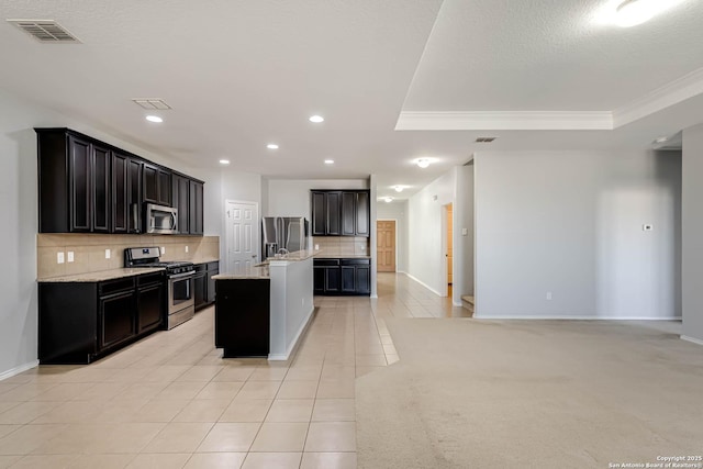 kitchen featuring a center island with sink, a raised ceiling, light stone countertops, appliances with stainless steel finishes, and light tile patterned flooring