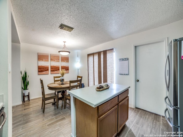 kitchen featuring stainless steel fridge, a center island, hanging light fixtures, and a textured ceiling