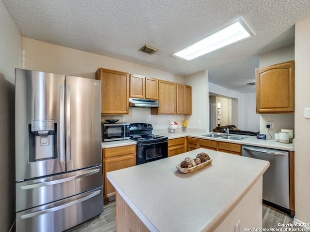 kitchen featuring a textured ceiling, a center island, stainless steel appliances, and sink