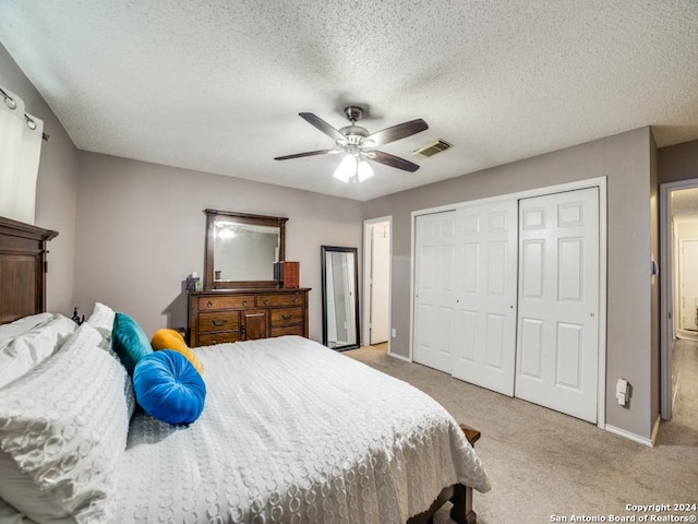 bedroom with ceiling fan, a closet, light carpet, and a textured ceiling