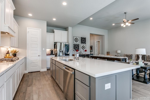 kitchen featuring appliances with stainless steel finishes, light wood-type flooring, sink, gray cabinets, and an island with sink