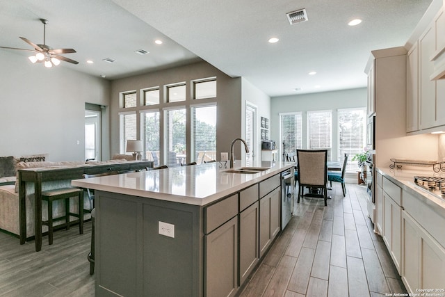 kitchen with ceiling fan, sink, stainless steel appliances, a breakfast bar area, and a center island with sink