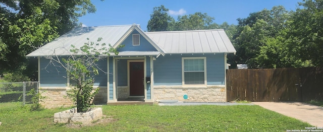 view of front of property with stone siding, a front lawn, a standing seam roof, and fence