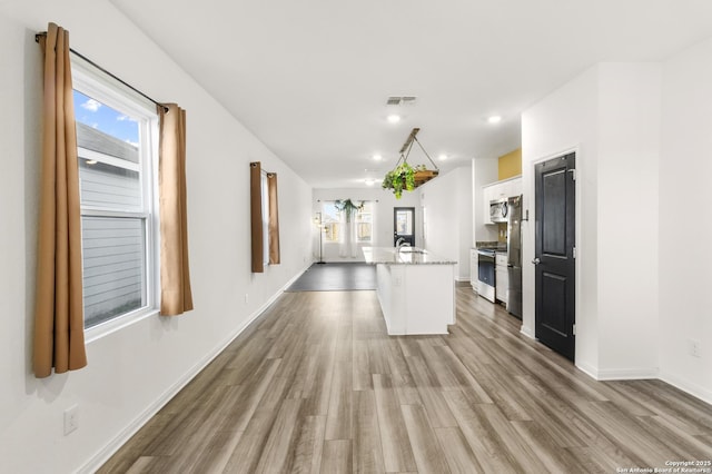 kitchen with an island with sink, a wealth of natural light, light hardwood / wood-style floors, white cabinetry, and stainless steel appliances