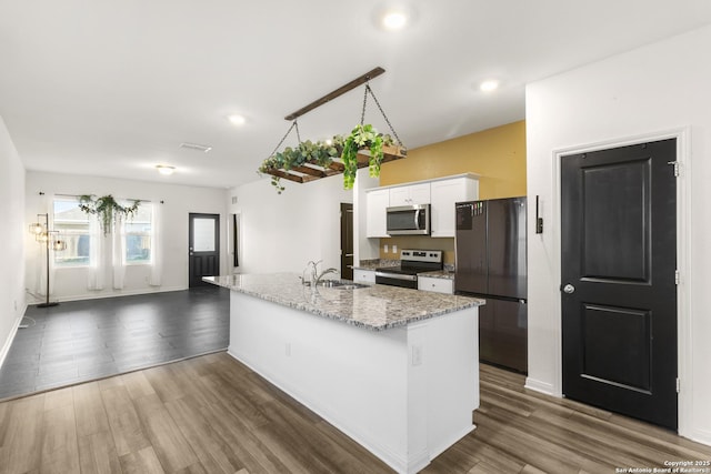 kitchen with dark hardwood / wood-style flooring, light stone counters, stainless steel appliances, a center island with sink, and white cabinetry