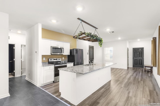 kitchen with white cabinets, appliances with stainless steel finishes, a kitchen island with sink, and sink