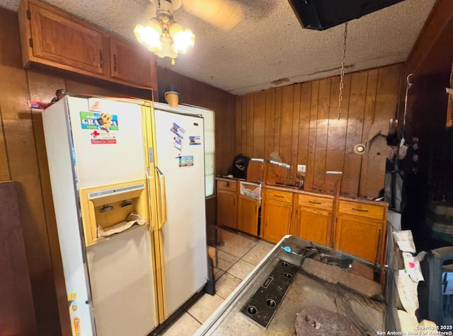 kitchen with a textured ceiling, ceiling fan, wooden walls, light tile patterned floors, and white fridge with ice dispenser