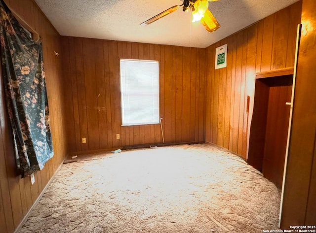 carpeted spare room featuring ceiling fan, wood walls, and a textured ceiling