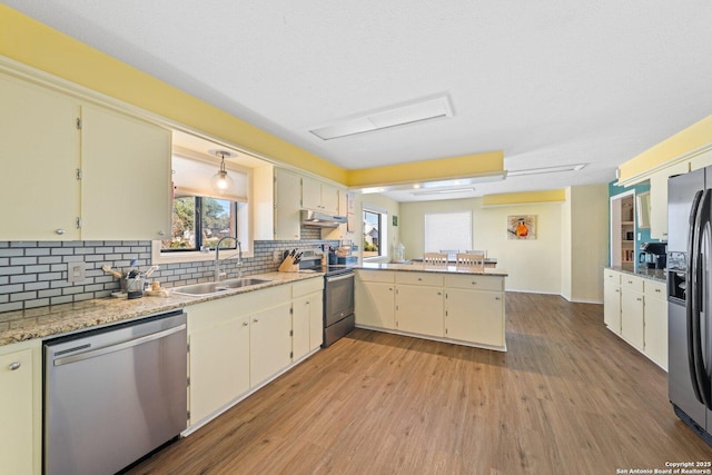 kitchen with sink, stainless steel appliances, kitchen peninsula, plenty of natural light, and light hardwood / wood-style floors