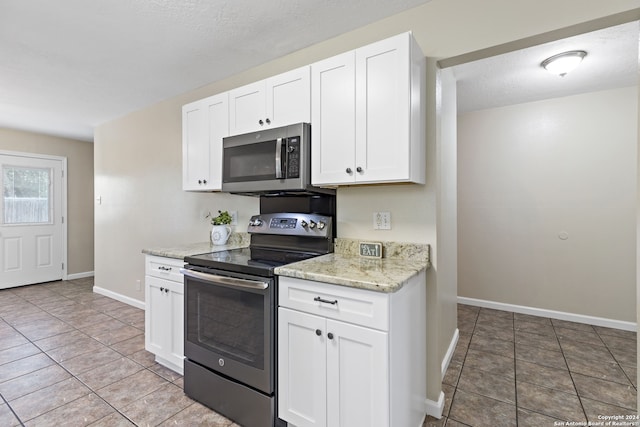 kitchen with light stone countertops, appliances with stainless steel finishes, light tile patterned floors, and white cabinetry