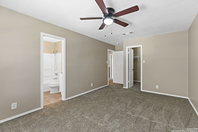 unfurnished bedroom with ceiling fan, dark colored carpet, ensuite bathroom, a walk in closet, and a closet