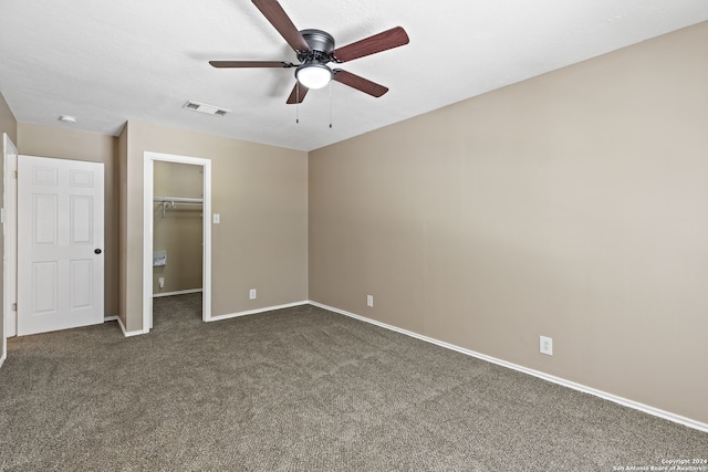 unfurnished bedroom featuring ceiling fan, a closet, dark carpet, and a spacious closet