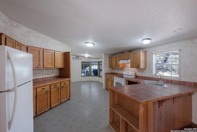 kitchen with white appliances, lofted ceiling, sink, tile counters, and kitchen peninsula