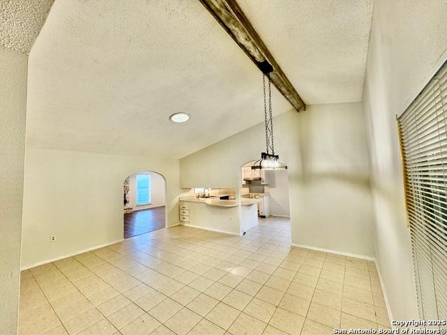 interior space featuring sink, light tile patterned flooring, lofted ceiling with beams, and a textured ceiling