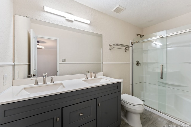 bathroom with vanity, a textured ceiling, a shower with door, hardwood / wood-style floors, and toilet