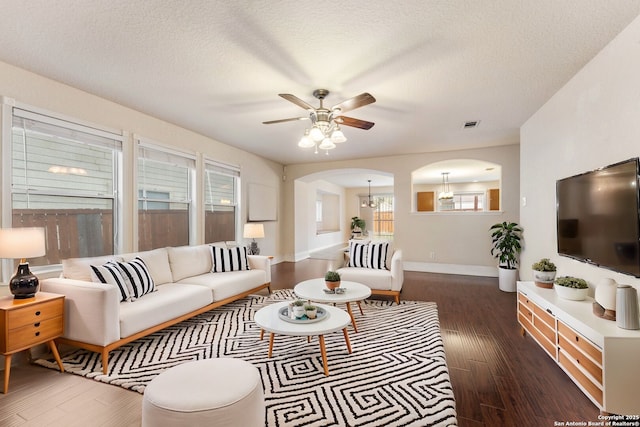 living room with a textured ceiling, a wealth of natural light, ceiling fan with notable chandelier, and dark hardwood / wood-style floors