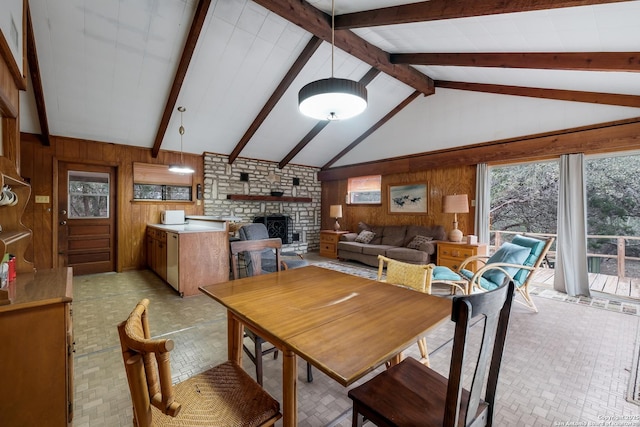 dining room featuring vaulted ceiling with beams, a fireplace, and wooden walls