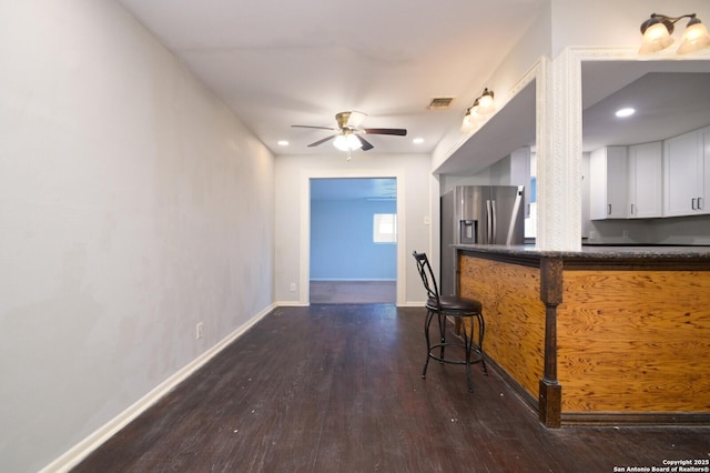 kitchen with ceiling fan, dark wood-type flooring, a kitchen breakfast bar, stainless steel fridge with ice dispenser, and white cabinets