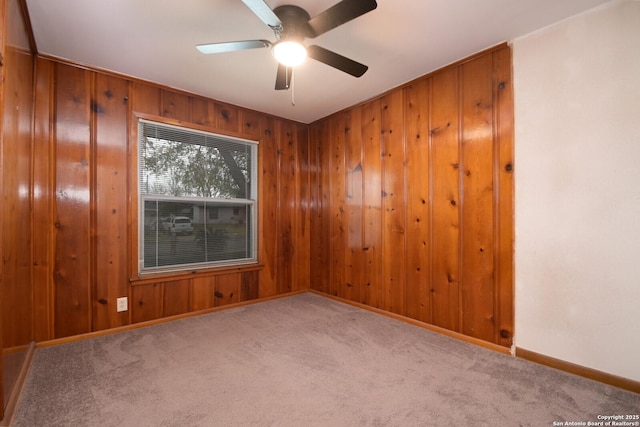 carpeted spare room featuring ceiling fan and wood walls