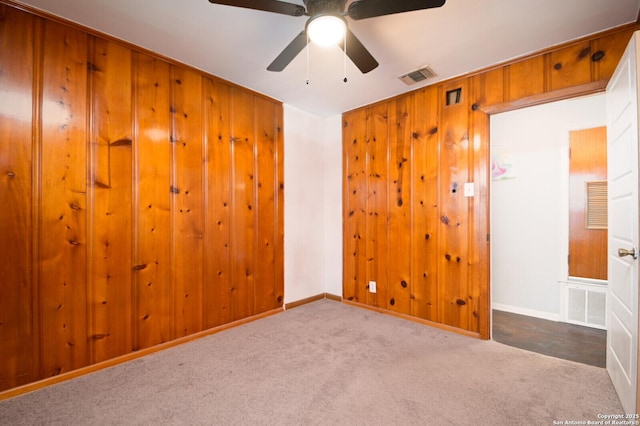 spare room featuring carpet flooring, wood walls, and ceiling fan