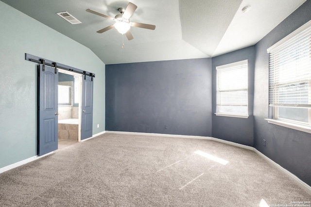 unfurnished bedroom featuring carpet floors, vaulted ceiling, ceiling fan, and a barn door