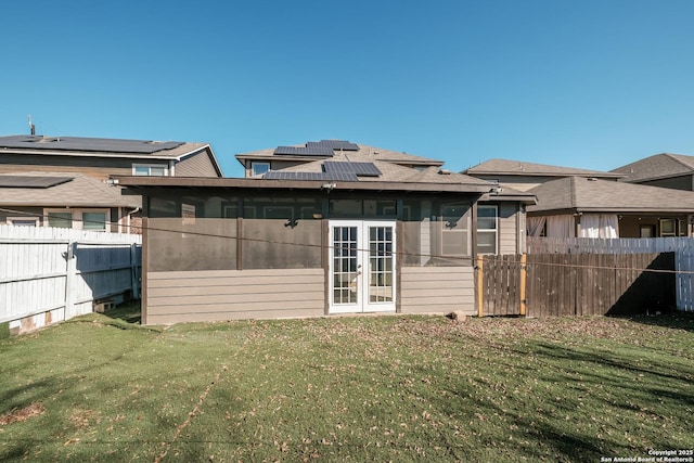 back of property featuring french doors, solar panels, and a lawn