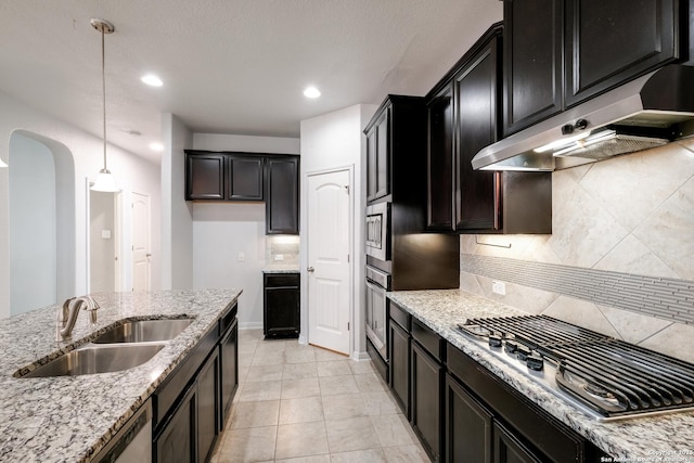 kitchen with backsplash, sink, hanging light fixtures, light stone counters, and stainless steel appliances