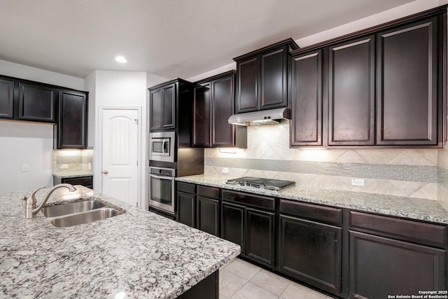 kitchen featuring appliances with stainless steel finishes, tasteful backsplash, light stone counters, sink, and light tile patterned floors