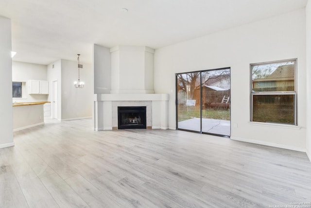 unfurnished living room with a tiled fireplace, a chandelier, and light hardwood / wood-style floors