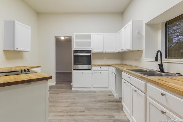 kitchen featuring stainless steel oven, sink, butcher block countertops, white cabinets, and light wood-type flooring