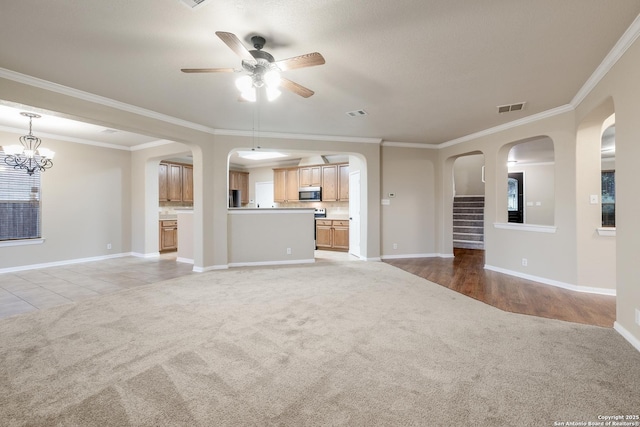 unfurnished living room with light colored carpet, ceiling fan with notable chandelier, and ornamental molding