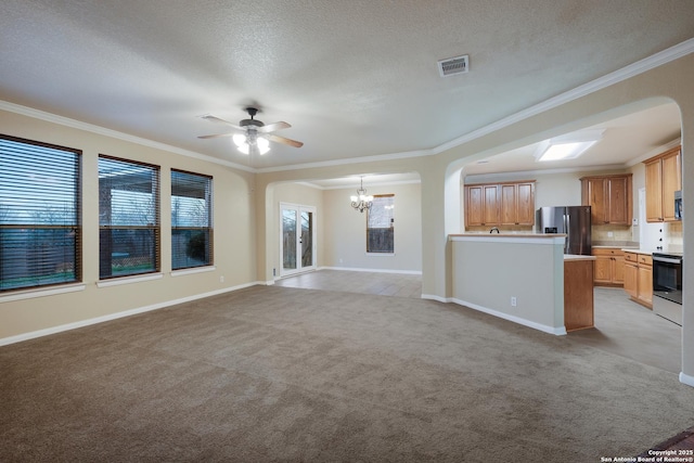 unfurnished living room featuring a textured ceiling, ceiling fan with notable chandelier, light colored carpet, and ornamental molding