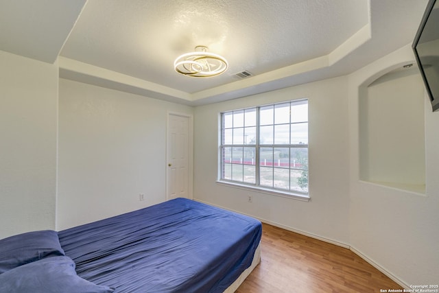 bedroom featuring wood-type flooring, a textured ceiling, and a tray ceiling