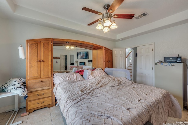 bedroom featuring white refrigerator, a tray ceiling, ceiling fan, and light tile patterned flooring