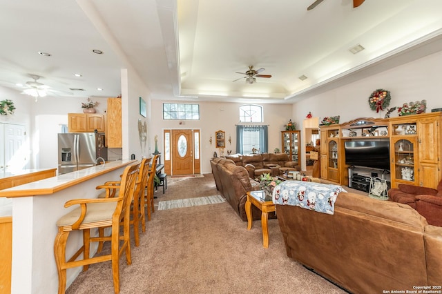 carpeted living room with ceiling fan and a tray ceiling