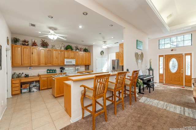 kitchen featuring white appliances, ceiling fan, a center island, a kitchen bar, and light carpet