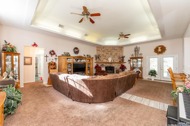 living room with light carpet, a fireplace, ceiling fan, and a tray ceiling