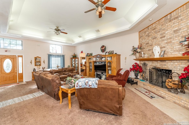 carpeted living room featuring a tray ceiling, a fireplace, and ceiling fan