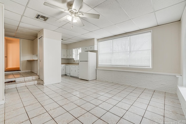 unfurnished living room featuring ceiling fan, a drop ceiling, and light tile patterned floors