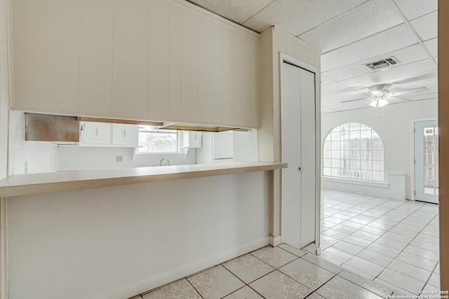 kitchen with a drop ceiling, ceiling fan, light tile patterned floors, white fridge, and kitchen peninsula