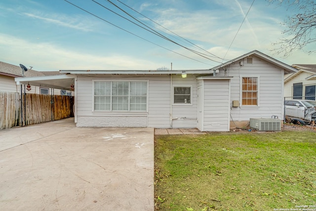 rear view of house with central air condition unit, a carport, and a lawn