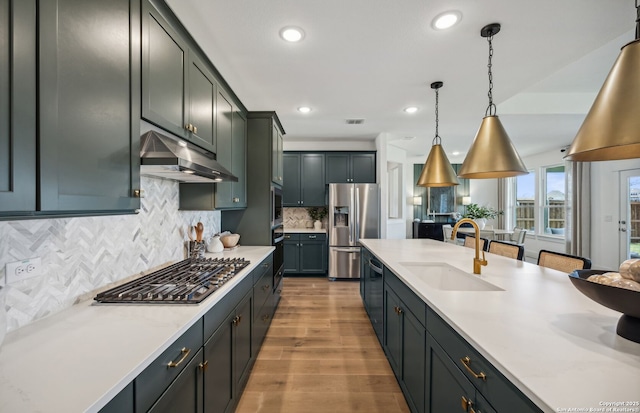 kitchen with hanging light fixtures, sink, light hardwood / wood-style flooring, appliances with stainless steel finishes, and tasteful backsplash